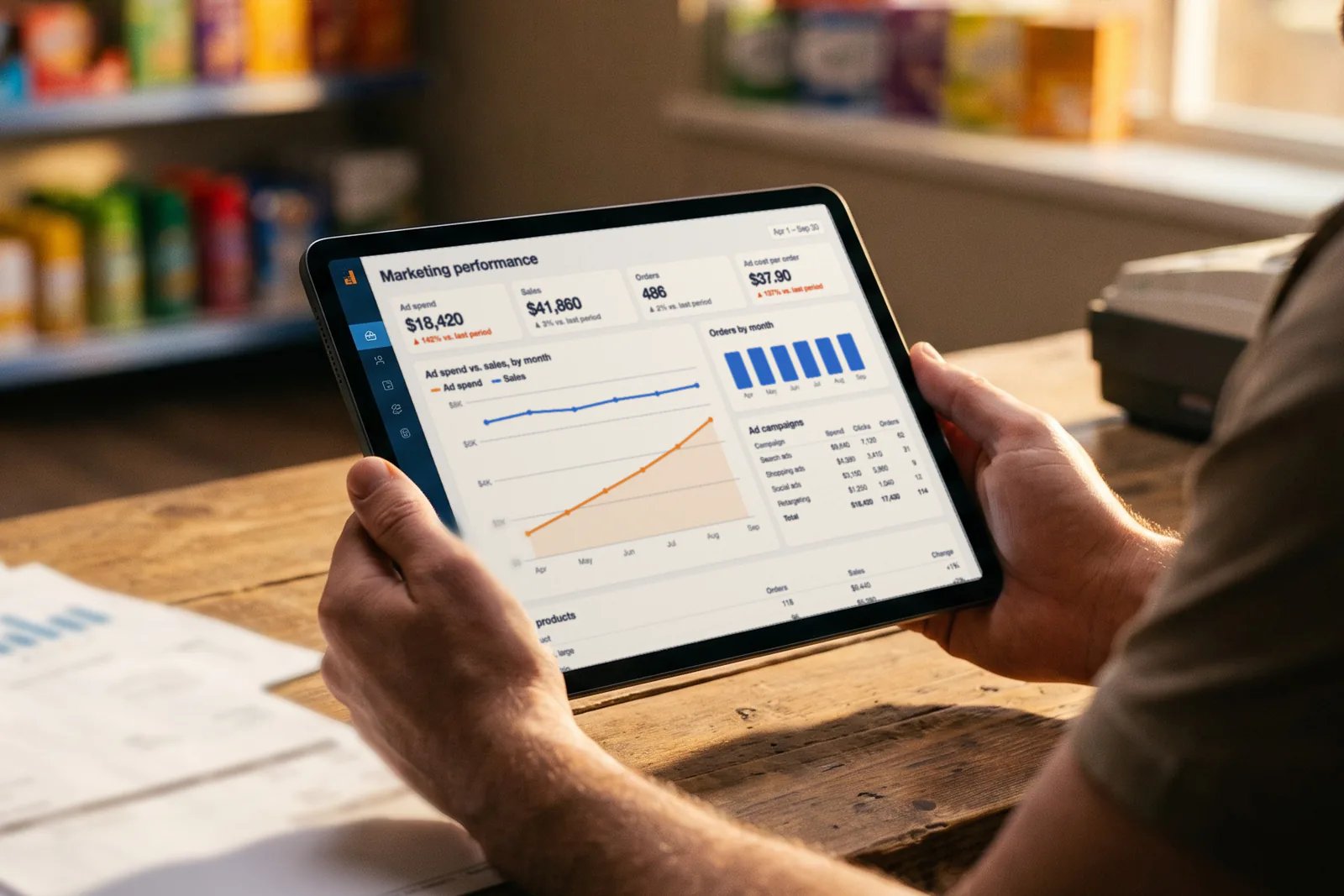 A shop owner at an empty counter reviews a tablet dashboard where ad spend keeps climbing while sales stay flat