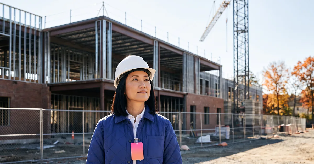 Construction business development manager in a hard hat looking over a school building under construction
